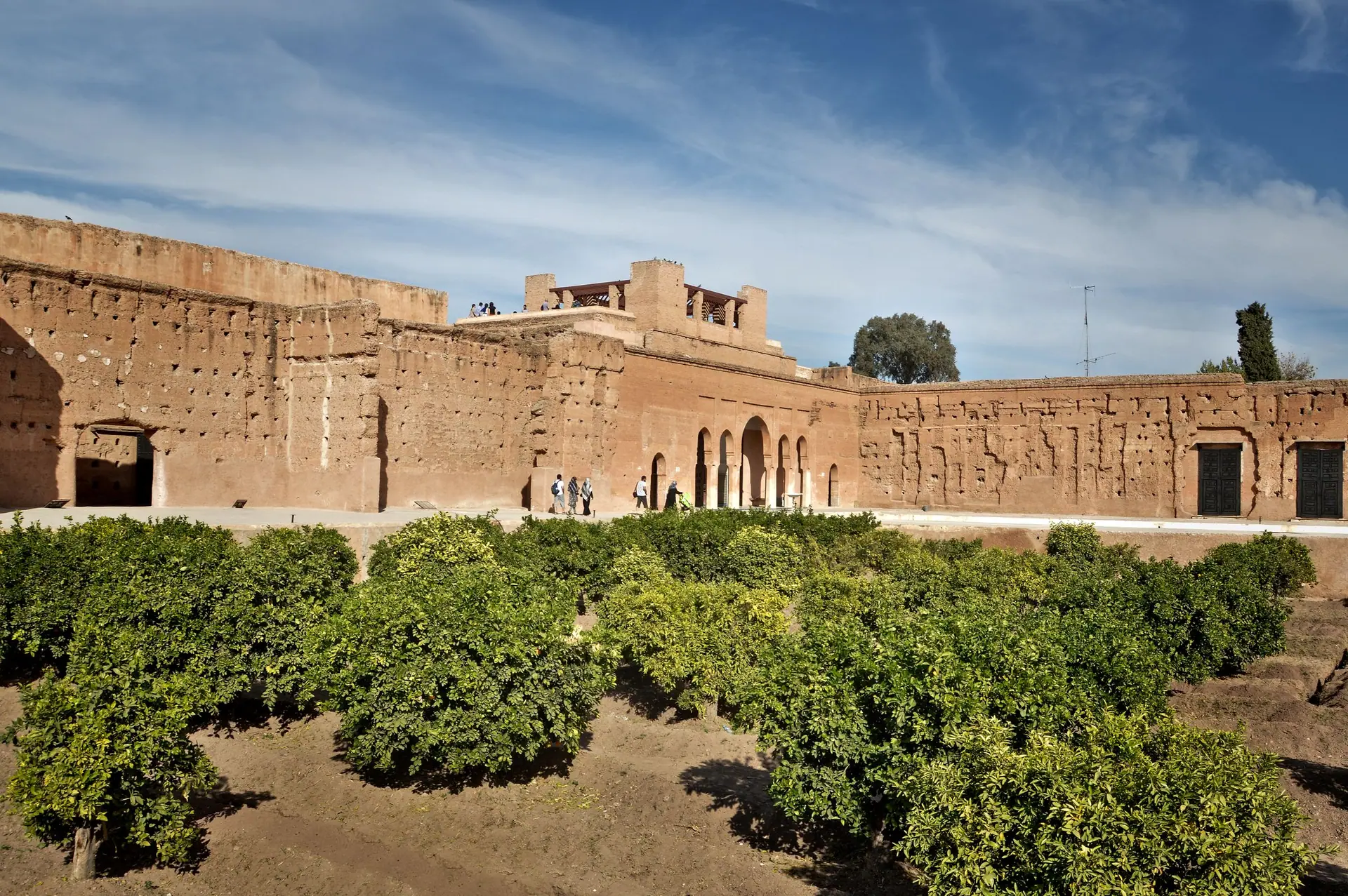 View of historic red walls and lush gardens under a blue sky in Marrakesh, Morocco.
